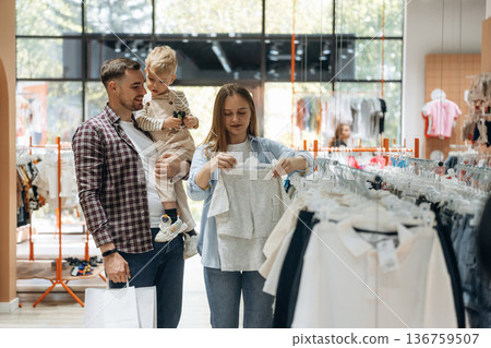 Holding boy in hands. Father, son and pregnant mother are in kid's clothing store Holding boy in hands. Father, son and pregnant mother are in kid's clothing store 136759507