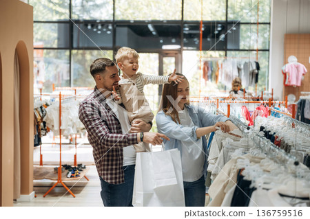 Bunch of wear hanging. Father, son and pregnant mother are in kid's clothing store Bunch of wear hanging. Father, son and pregnant mother are in kid's clothing store 136759516