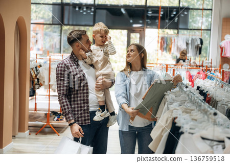 Bunch of wear hanging. Father, son and pregnant mother are in kid's clothing store 136759518