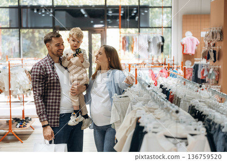 Bunch of wear hanging. Father, son and pregnant mother are in kid's clothing store Bunch of wear hanging. Father, son and pregnant mother are in kid's clothing store 136759520