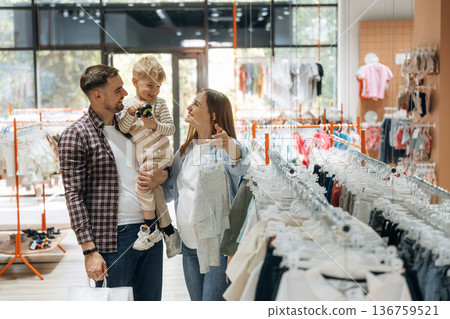 Asking if child like that wear. Father, son and pregnant mother are in kid's clothing store Asking if child like that wear. Father, son and pregnant mother are in kid's clothing store 136759521
