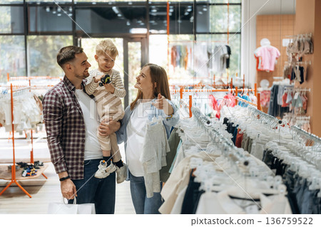 Conception of love and care. Father, son and pregnant mother are in kid's clothing store Conception of love and care. Father, son and pregnant mother are in kid's clothing store 136759522