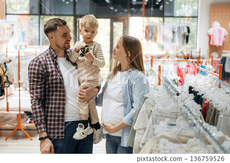 Conception of love and care. Father, son and pregnant mother are in kid's clothing store 136759526