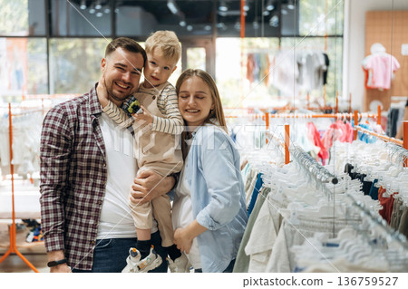 Standing and smiling. Father, son and pregnant mother are in kid's clothing store Standing and smiling. Father, son and pregnant mother are in kid's clothing store 136759527