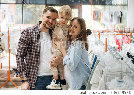 Standing and smiling. Father, son and pregnant mother are in kid's clothing store Standing and smiling. Father, son and pregnant mother are in kid's clothing store 136759528