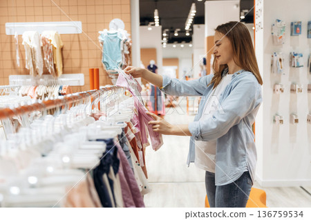 The cute little wear. Young pregnant woman is in the kid's clothing store The cute little wear. Young pregnant woman is in the kid's clothing store 136759534