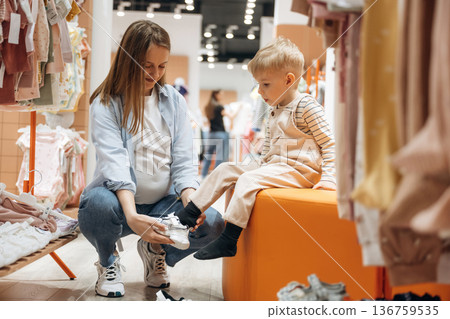 Sitting and trying new shoes. Young mother with her little baby son in the kid's clothing store Sitting and trying new shoes. Young mother with her little baby son in the kid's clothing store 136759535
