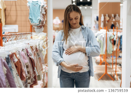 With belly. Young pregnant woman is in the kid's clothing store With belly. Young pregnant woman is in the kid's clothing store 136759539