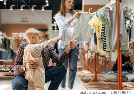 Choosing the wear. Father, son and pregnant mother are in kid's clothing store Choosing the wear. Father, son and pregnant mother are in kid's clothing store 136759674