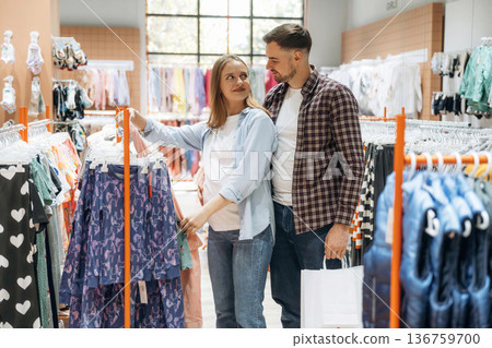 By the sweaters. Pregnant woman with man are in the kid's clothing store By the sweaters. Pregnant woman with man are in the kid's clothing store 136759700