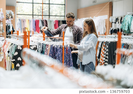 Together in the in the kid's clothing store. Pregnant woman with man Together in the in the kid's clothing store. Pregnant woman with man 136759703