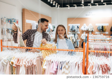 Cheerful facial expression. Pregnant woman with man are in the kid's clothing store Cheerful facial expression. Pregnant woman with man are in the kid's clothing store 136759716