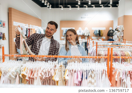 Cheerful facial expression. Pregnant woman with man are in the kid's clothing store Cheerful facial expression. Pregnant woman with man are in the kid's clothing store 136759717