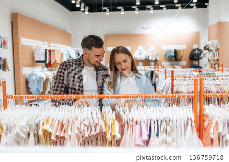 Cheerful facial expression. Pregnant woman with man are in the kid's clothing store Cheerful facial expression. Pregnant woman with man are in the kid's clothing store 136759718