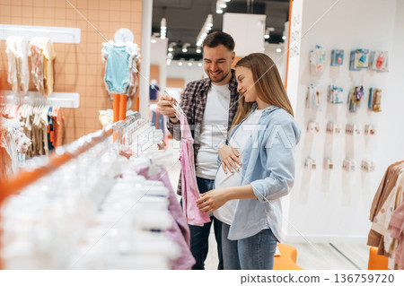 Clothes hanging in a row. Pregnant woman with man are in the kid's store Clothes hanging in a row. Pregnant woman with man are in the kid's store 136759720
