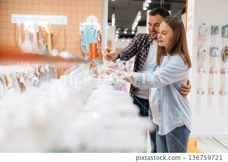 Clothes hanging in a row. Pregnant woman with man are in the kid's store 136759721