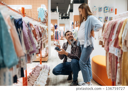 Shoes for child. Pregnant woman with man are in the kid's clothing store Shoes for child. Pregnant woman with man are in the kid's clothing store 136759727
