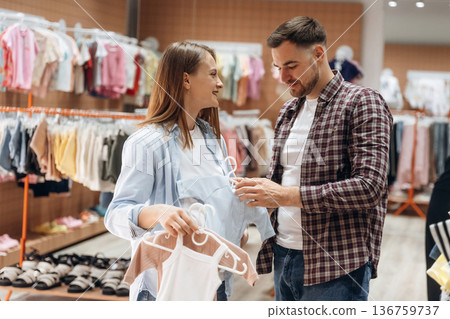 Many objects, wear, clothes. Pregnant woman with man are in the kid's clothing store Many objects, wear, clothes. Pregnant woman with man are in the kid's clothing store 136759737
