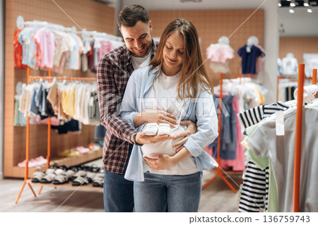 White cute little shoes. Pregnant woman with man are in the kid's clothing store White cute little shoes. Pregnant woman with man are in the kid's clothing store 136759743