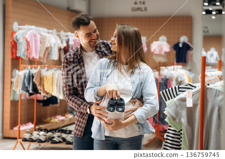 Shoes for child. Pregnant woman with man are in the kid's clothing store Shoes for child. Pregnant woman with man are in the kid's clothing store 136759745