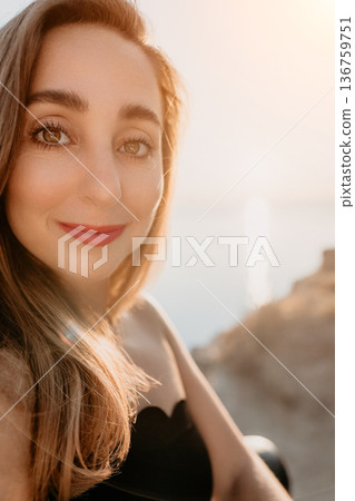 Woman portrait sunset smiling during golden hour on a coast overlooking the sea with warm natural light 136759751