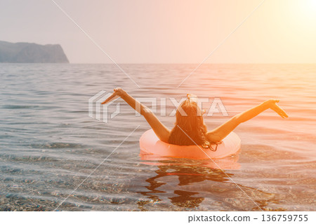 Woman ocean inflatable floating in calm sea with arms outstretched during a golden sunset reflecting vacation and freedom Woman ocean inflatable floating in calm sea with arms outstretched during a golden sunset reflecting vacation and freedom 136759755