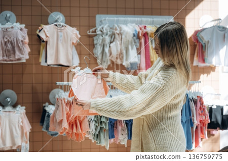 Woman is choosing wear in the kid's clothing store Woman is choosing wear in the kid's clothing store 136759775