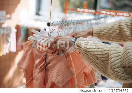 Pink colored. Woman is choosing wear in the kid's clothing store Pink colored. Woman is choosing wear in the kid's clothing store 136759782