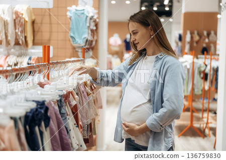 Hand is on the abdomen. Young pregnant woman is in the kid's clothing store Hand is on the abdomen. Young pregnant woman is in the kid's clothing store 136759830