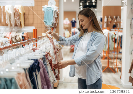 The cute little wear. Young pregnant woman is in the kid's clothing store The cute little wear. Young pregnant woman is in the kid's clothing store 136759831