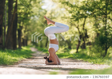 Gymnastics concept, doing headstand. Beautiful fitness yoga woman is outdoors, amazing nature 136760397