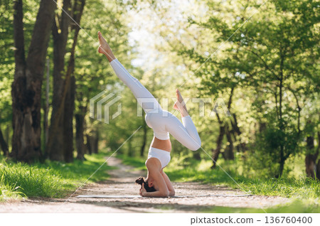 Doing headstand. Beautiful fitness yoga woman is outdoors, amazing nature 136760400