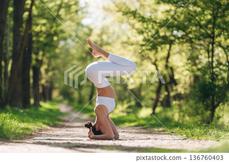 Doing headstand. Beautiful fitness yoga woman is outdoors, amazing nature 136760403