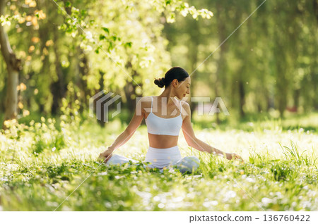 Feeling good, sitting on the grass and doing exercise. Beautiful fitness yoga woman is outdoors, amazing nature 136760422