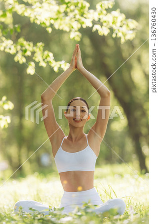 Arms raised up, sitting on the grass. Beautiful fitness yoga woman is outdoors, amazing nature Arms raised up, sitting on the grass. Beautiful fitness yoga woman is outdoors, amazing nature 136760430