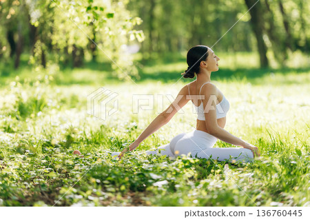 Side view, sitting on the grass. Beautiful fitness yoga woman is outdoors, amazing nature 136760445