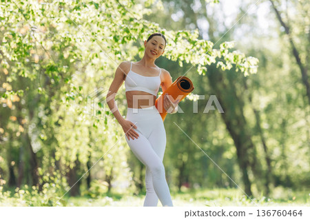 Ready for practice, standing and holding mat. Beautiful fitness yoga woman is outdoors, amazing nature Ready for practice, standing and holding mat. Beautiful fitness yoga woman is outdoors, amazing nature 136760464