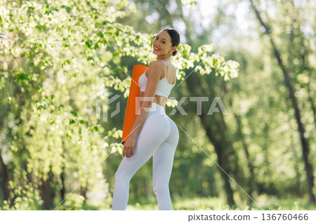 Ready for practice, standing and holding mat. Beautiful fitness yoga woman is outdoors, amazing nature Ready for practice, standing and holding mat. Beautiful fitness yoga woman is outdoors, amazing nature 136760466
