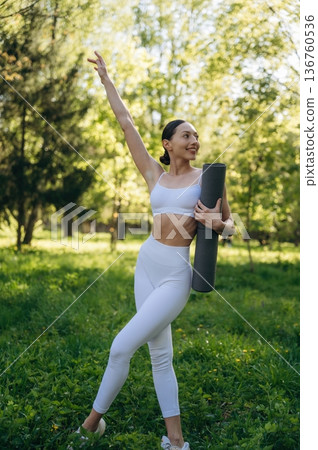 Holding yoga mat. Beautiful fitness woman is outdoors, amazing nature Holding yoga mat. Beautiful fitness woman is outdoors, amazing nature 136760536