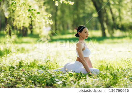 Side view, sitting on the grass. Beautiful fitness yoga woman is outdoors, amazing nature Side view, sitting on the grass. Beautiful fitness yoga woman is outdoors, amazing nature 136760656