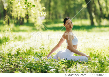 Side view, sitting on the grass. Beautiful fitness yoga woman is outdoors, amazing nature 136760658