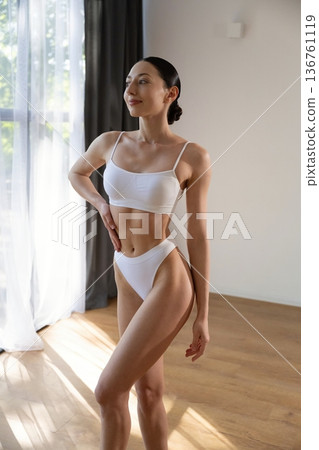 Near the window, sunlight. Young woman in fitness clothes is in the room 136761119