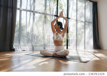 Lotus pose, sitting. Young woman in fitness clothes is in the room Lotus pose, sitting. Young woman in fitness clothes is in the room 136761329