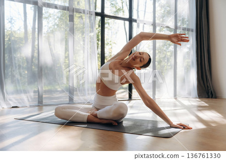 Spine exercise, hand to the side. Young woman in fitness clothes is in the room Spine exercise, hand to the side. Young woman in fitness clothes is in the room 136761330