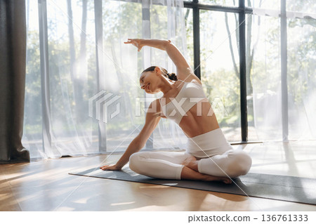 Spine exercise, hand to the side. Young woman in fitness clothes is in the room Spine exercise, hand to the side. Young woman in fitness clothes is in the room 136761333