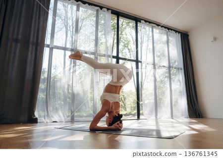 Upside down, headstand. Young woman in fitness clothes is in the room Upside down, headstand. Young woman in fitness clothes is in the room 136761345