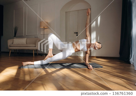 Shadow and sunlight, doing yoga. Young woman in fitness clothes is in the room Shadow and sunlight, doing yoga. Young woman in fitness clothes is in the room 136761360