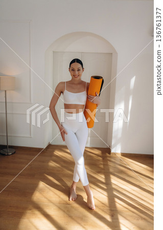 Hobby of yoga, standing and holding the mat. Young woman in fitness clothes is in the room Hobby of yoga, standing and holding the mat. Young woman in fitness clothes is in the room 136761377