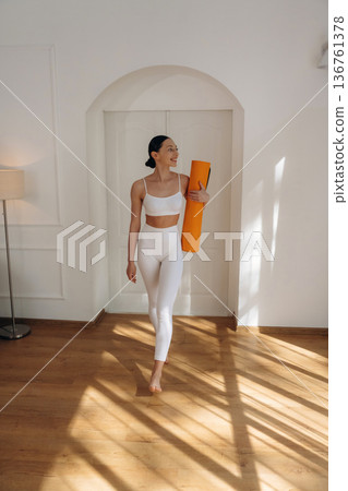 Daily practice routine, with yoga mat. Young woman in fitness clothes is in the room Daily practice routine, with yoga mat. Young woman in fitness clothes is in the room 136761378