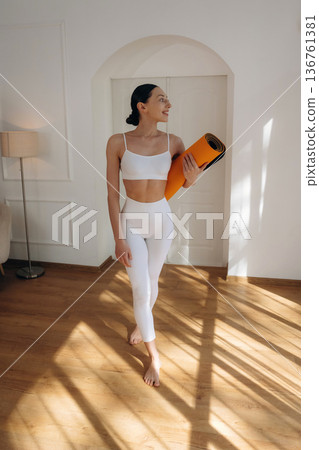 Daily practice routine, with yoga mat. Young woman in fitness clothes is in the room Daily practice routine, with yoga mat. Young woman in fitness clothes is in the room 136761381